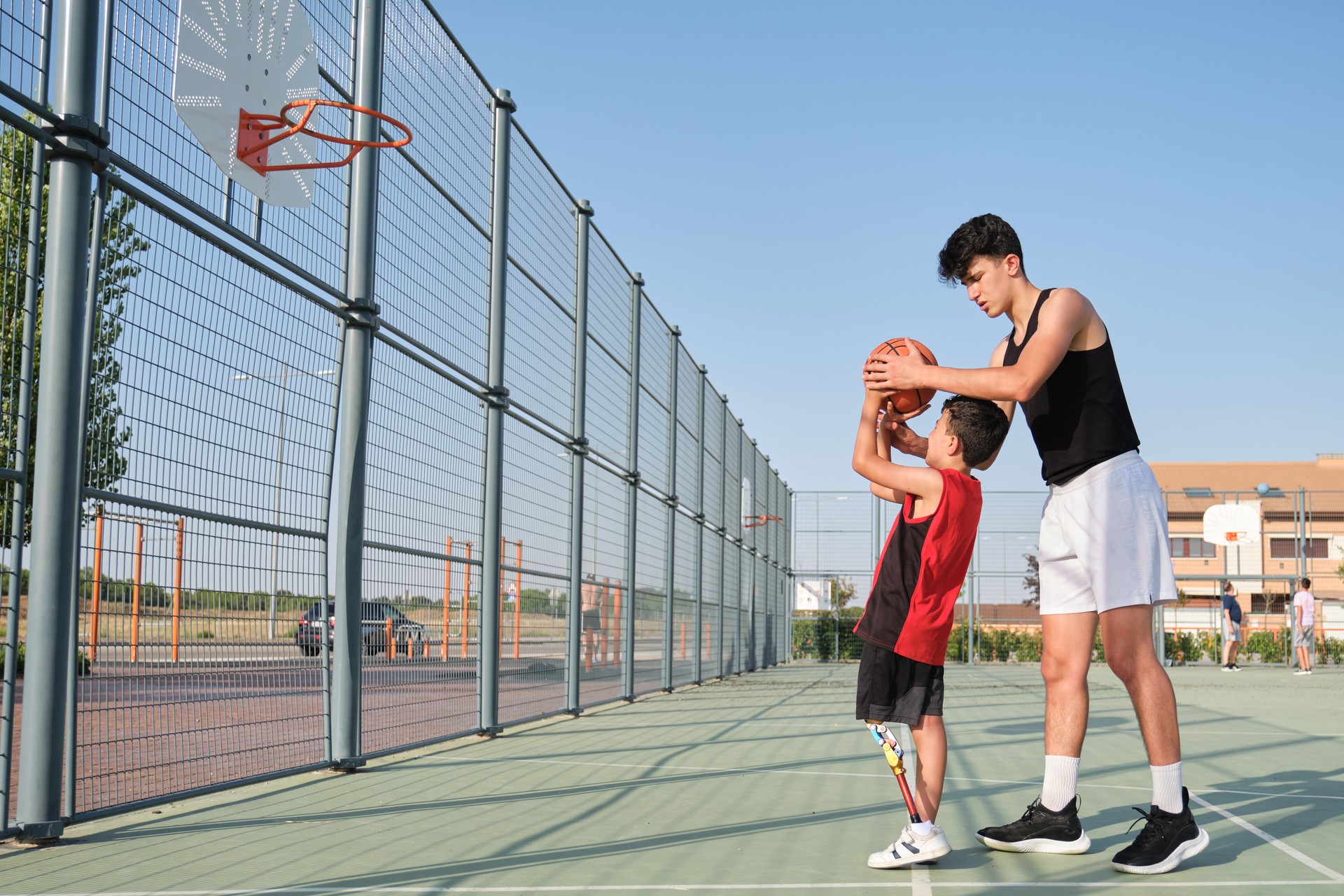 Basketball trainer showing how to shoot basketball to a child with a leg prosthesis. Coach training a kid.